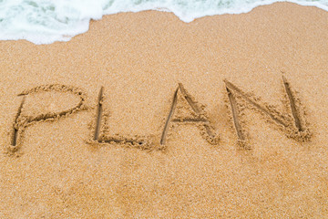 PLAN inscription written on sandy beach with wave approaching