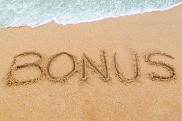 BONUS inscription written on sandy beach with wave approaching