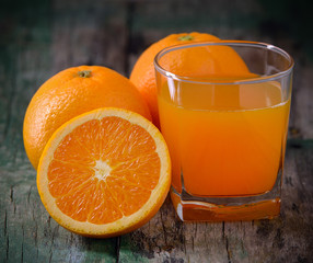 Orange juice glass and fresh oranges on wood