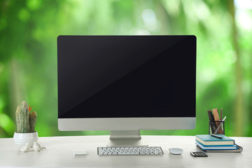Computer on wooden table on nature green background