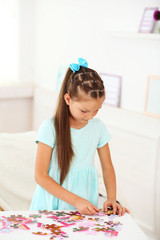 Cute little girl playing with puzzles on home interior background