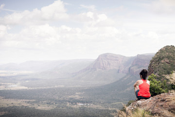 Fototapeta premium Young woman sitting at edge of cliff looking over expansive view