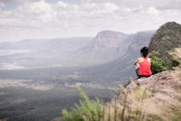 Obraz premium Young woman sitting at edge of cliff looking over expansive view
