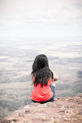 Young woman sitting at edge of cliff looking over expansive view