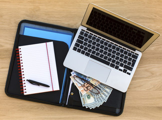 Business background - detailed business case with laptop, open notebook and dollars/euros bills. Top view of wooden texture of the table.