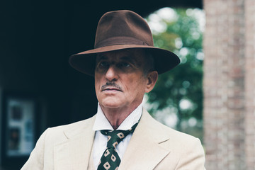 Close-up of senior dandy with hat and suit in front of gate.