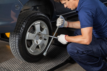 Obraz premium Mechanic Using Rim Wrench To Tighten Car Tire