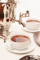 On the white tablecloth is a samovar, a teapot, a cup of tea and sweets, biscuits, rolls, tea,