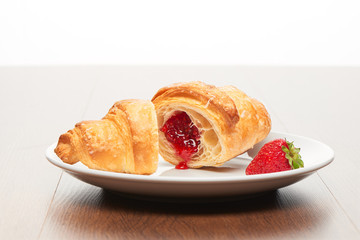 Fresh french croissant with strawberry jam filling cut into two pieces and strawberry on white...