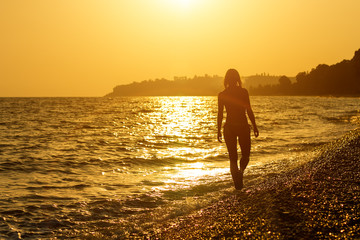 Fototapeta premium The girl goes on a beach at sunset