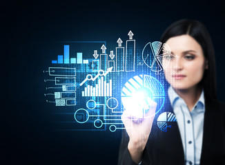 A business woman in formal suit is pushing out the element on the hologram with business icons. Dark background.