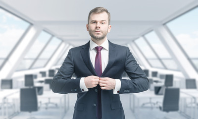 Fototapeta premium A handsome professional is buttoning up the suit. Bright modern panoramic roof loft office. The concept of luxury consulting services.