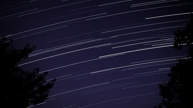 Star Trails. the night sky revealing star trails. trees on either side.
