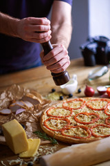 Man's hands salting cooked Italian pizza