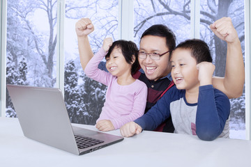 Two kids and dad raise hands while using laptop