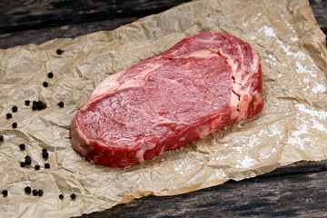 Raw rib eye steak on crumpled paper, pepper, salt.