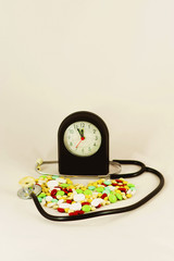 Tablets, medicines arranged in the form of heart with a stethoscope and a clock - obrazy, fototapety, plakaty