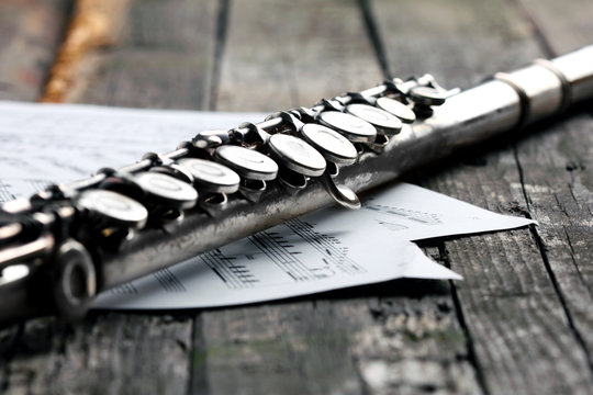 Old silver flute and music notes on rusty table