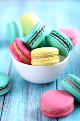 Tasty colorful macarons in bowl on a blue wooden table