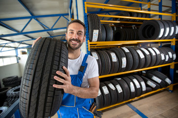 smiling auto mechanic carrying tire