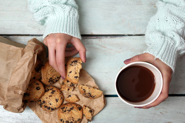 Female hands holding cup of coffee and cookies on wooden table close up