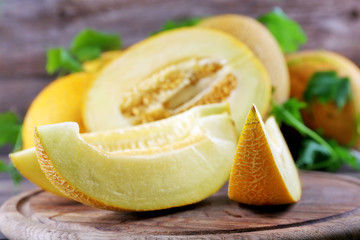 Ripe melons with green leaves on wooden table close up