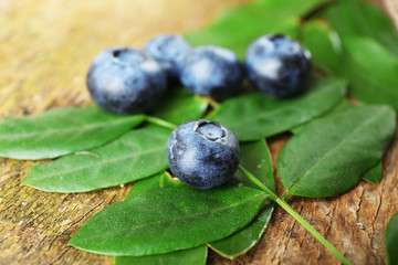 Fresh blueberries with green leaves on wooden table, closeup