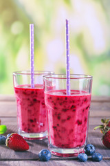 Glasses of berry smoothie on wooden table on blurred background