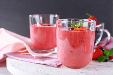 Glasses of berry smoothie on wooden table on dark background