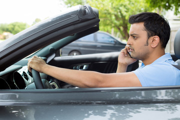Closeup portrait, sad handsome young man in blue polo shirt sitting, driving in gray black sports car on cellphone with bad news, isolated outdoors background