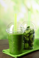 Green vegetable and fruit salad and healthy fresh drink in plastic cups on bright background. Colorful diet concept