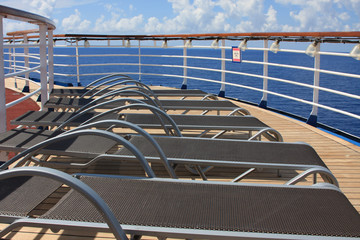 Pool chairs in a row on deck onboard a cruise ship at sea