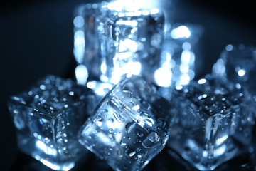 Shining ice cubes under blue light on liquid background