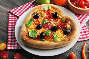 Heart shaped pizza served on plate on wooden background