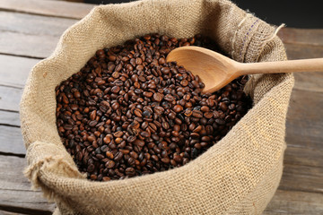 Sac with roasted coffee beans with spoon on wooden background