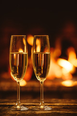 Two glasses of sparkling champagne in front of warm fireplace. Cozy relaxed magical atmosphere in a chalet house by the fireside. Snug holiday concept. Beautiful background with shimmering wine.