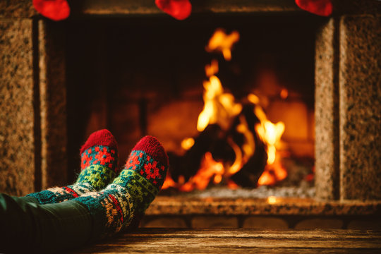 Feet in woollen socks by the fireplace. Woman relaxes by warm fire and warming up her feet in woollen socks. Close up on feet. Winter and Christmas holidays concept.
