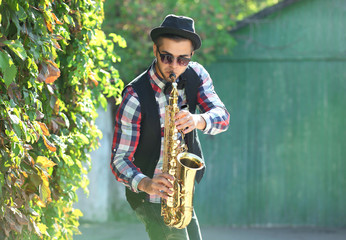 Young man playing on saxophone outside near the old wall