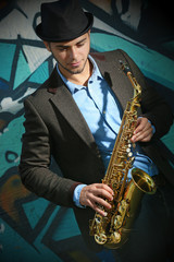 Plakat Young man with saxophone outside near the old painted wall