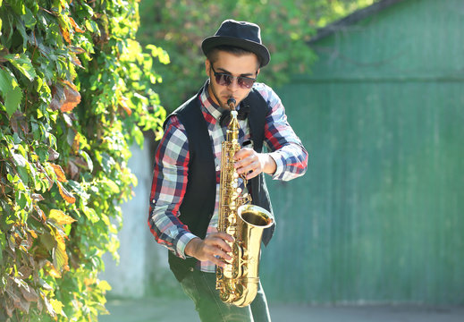 Young man playing on saxophone outside near the old wall