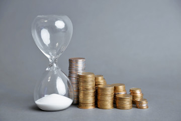Hourglass with coins on gray background