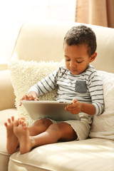 Little boy sitting on sofa with tablet in the room