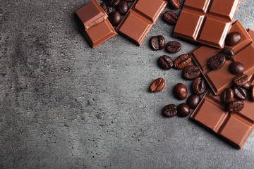 Milk chocolate pieces and coffee grains on gray background