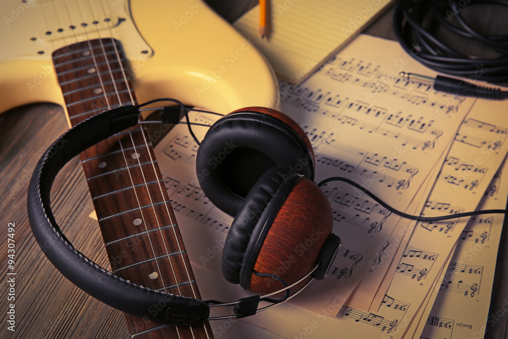 Wall mural Electric guitar with headphones and musical notes on wooden background