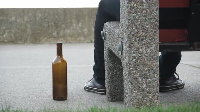 Man depressed with wine bottle sitting on bench outdoor 4K