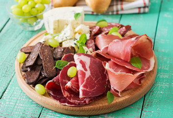 Antipasto catering platter with bacon, jerky, sausage, blue cheese and grapes on a wooden background