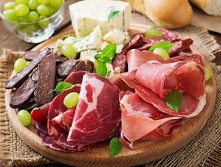 Antipasto catering platter with bacon, jerky, sausage, blue cheese and grapes on a wooden background