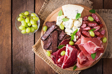 Antipasto catering platter with bacon, jerky, sausage, blue cheese and grapes on a wooden background