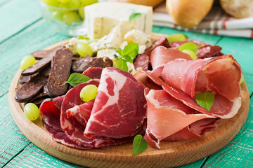 Antipasto catering platter with bacon, jerky, sausage, blue cheese and grapes on a wooden background