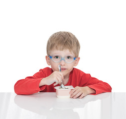 The five-year-old boy sits at a white table and eats yogurt,  isolated on a white background